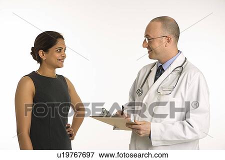 Stock Photo - Caucasian mid adult male physician talking with Indian woman patient.. Fotosearch