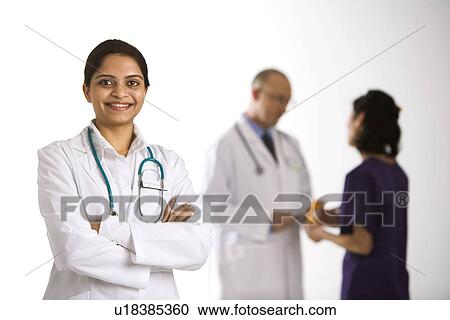 Indian mid adult woman doctor standing with medical staff in background. View Large Photo Image Stock Image - Indian mid adult woman doctor standing with medical staff in background.. Fotosearch