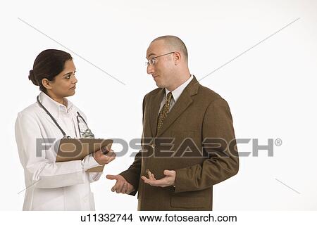 Indian mid adult woman doctor talking with man in business suit. View Large Photo Image Picture - Indian mid adult woman doctor talking with man in business suit.. Fotosearch