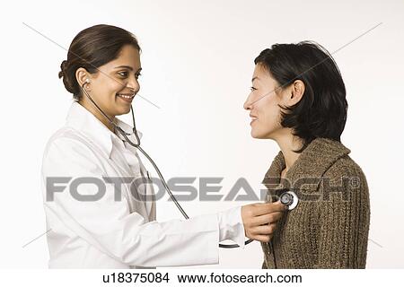 Indian woman doctor using stethescope on Asian woman patient. View Large Photo Image Picture - Indian woman doctor using stethescope on Asian woman patient.. Fotosearch