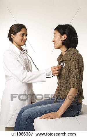 Indian woman doctor using stethescope on Asian woman patient. View Large Photo Image Stock Photo - Indian woman doctor using stethescope on Asian woman patient.. Fotosearch