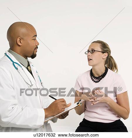 Mid-adult African-American doctor with clipboard and Caucasion mid-adult female patient in doctor's office looking at viewer and smiling. View Large Photo Image Stock Image - Mid-adult African-American doctor with clipboard and Caucasion mid-adult female patient in doctor's office looking at viewer and smiling.. Fotosearch