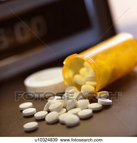 Stock Photo - Open medicine bottle with pills spilling out onto table with clock in background.. Fotosearch