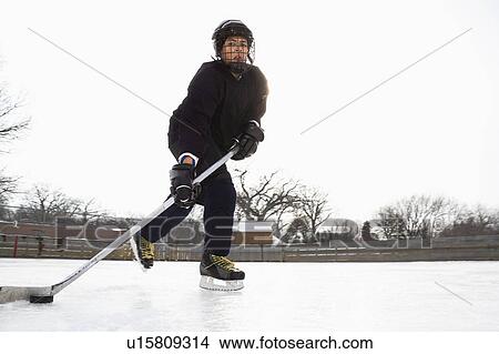 Picture - Boy in ice hockey uniform skating on ice rink moving puck.. Fotosearch