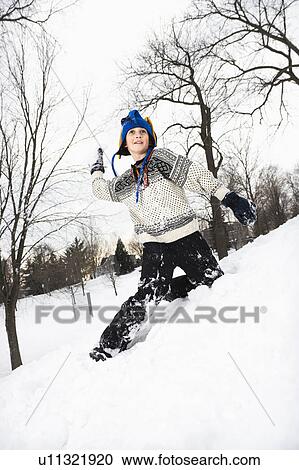 Stock Image - Boy wearing sweater and blue winter cap playing and throwing snow. Fotosearch