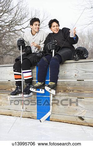Boys in ice hockey uniforms sitting on ice rink sidelines pointing and looking View Large Photo Image Stock Photograph - Boys in ice hockey uniforms sitting on ice rink sidelines pointing and looking. Fotosearch