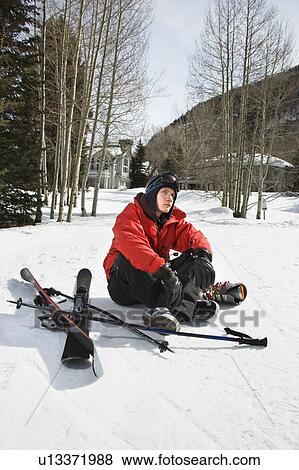 Stock Photo - Caucasian male teenager sitting on snow with ski gear.. Fotosearch