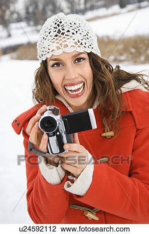 Caucasian young adult female in winter clothing holding video camera and smiling at viewer. View Large Photo Image Stock Image - Caucasian young adult female in winter clothing holding video camera and smiling at viewer.. Fotosearch