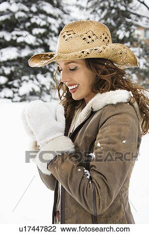 Stock Image - Caucasian young adult female outdoors in snow holding coffee cup and wearing straw cowboy hat.. Fotosearch