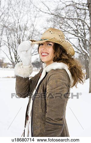 Picture - Caucasian young adult female smiling and tilting straw cowboy hat at viewer.. Fotosearch
