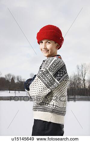 Stock Photo - Portrait of Caucasian boy wearing sweater and red winter cap standing looking over shoulder and smiling at viewer.. Fotosearch