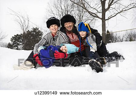 Stock Photo - Portrait of happy family of four sitting in snow smiling at viewer. Fotosearch