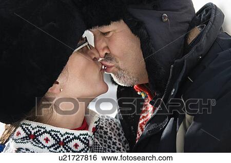 Stock Photograph - Side view of Caucasian middle aged man and woman in winter clothing kissing.. Fotosearch