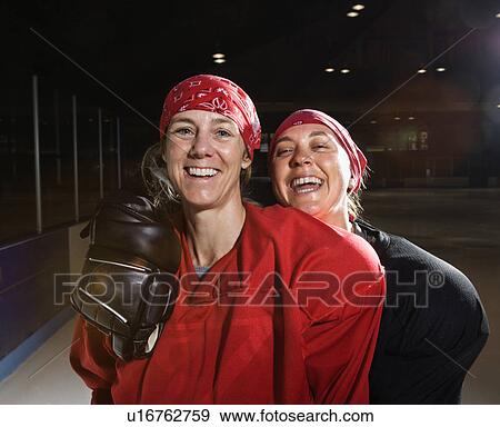 Stock Photo - Women hockey players in uniform posing with helmets off on ice rink. Fotosearch