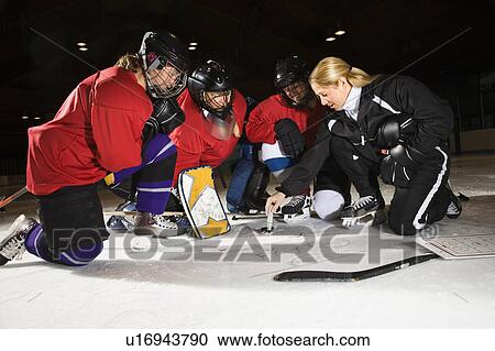 Stock Image - Women hockey players on ice looking at game plan with coach.. Fotosearch
