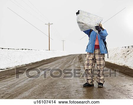 Young woman in winter clothes standing on muddy dirt road looking at map. View Large Photo Image Picture - Young woman in winter clothes standing on muddy dirt road looking at map.. Fotosearch