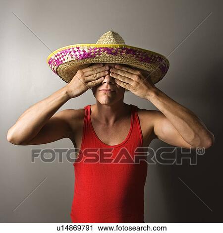 Stock Image - Portrait of a mid-adult Caucasian male wearing sombrero with hands over eyes.. Fotosearch