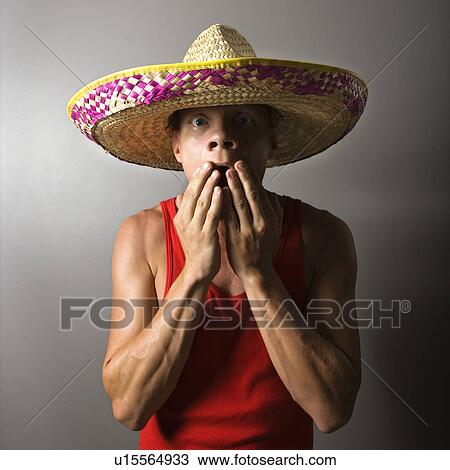 Stock Image - Portrait of a mid-adult male wearing sombrero with hands over mouth. Fotosearch