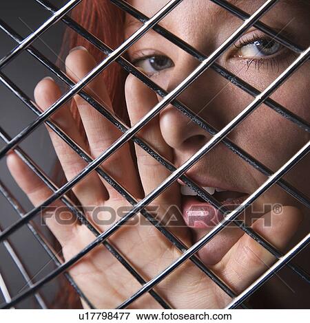 Stock Photo - Pretty redhead young woman face and hand behind metal pattern. Fotosearch