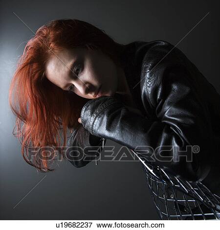 Stock Photo - Pretty redhead young woman wearing leather jacket hanging over back of chair. Fotosearch