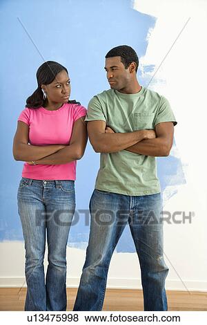 Stock Photo - African American couple glaring at each other with anger next to half-painted wall.. Fotosearch