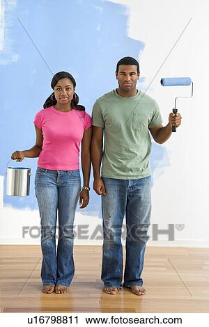 Stock Image - African American couple next to half-painted wall with paint supplies-American Gothic-style.. Fotosearch
