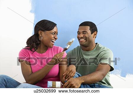 African American couple sitting and playing with paint brushes next to half-painted wall. View Large Photo Image Stock Photo - African American couple sitting and playing with paint brushes next to half-painted wall.. Fotosearch