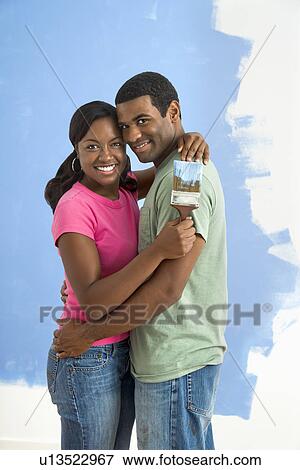 African American couple standing together hugging in front of half-painted wall and smiling at viewer. View Large Photo Image Stock Photo - African American couple standing together hugging in front of half-painted wall and smiling at viewer.. Fotosearch