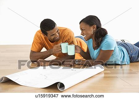 Stock Photo - African American male and female couple with architectural blueprints toasting with their coffee cups.. Fotosearch