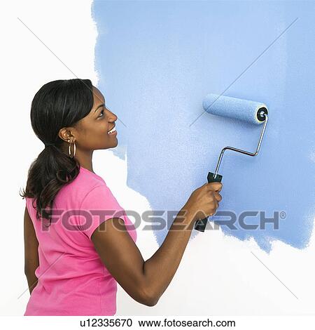 Stock Image - African American woman painting wall blue.. Fotosearch