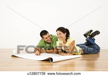 Attractive young adult couple laying on home floor with coffee cups smiling and looking at blueprints View Large Photo Image Stock Photo - Attractive young adult couple laying on home floor with coffee cups smiling and looking at blueprints. Fotosearch