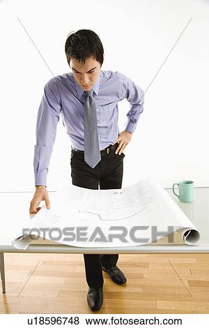 Business man standing looking over blueprints View Large Photo Image Stock Photo - Business man standing looking over blueprints. Fotosearch