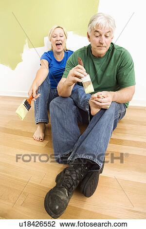 Stock Image - Couple in front of wall they are painting green while male tries to paint women's toenails with paintbrush. Fotosearch