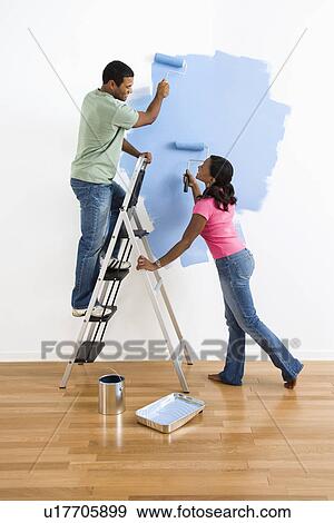 Stock Photo - Couple painting wall blue and smiling at each other. Fotosearch