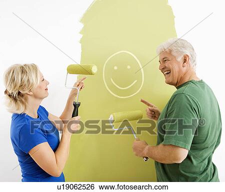 Stock Photograph - Couple painting wall green, finger-painting smiley face for fun. Fotosearch