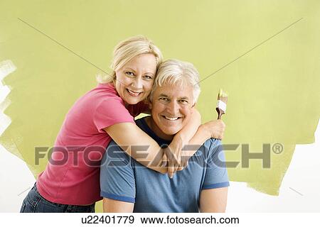 Stock Photo - Couple sitting in front of half-painted wall with paintbrushes. Fotosearch