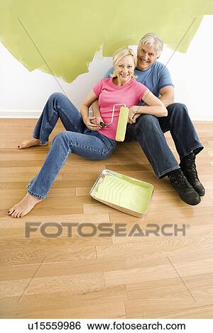Couple sitting in front of half-painted wall with paint supplies snuggling View Large Photo Image Stock Photograph - Couple sitting in front of half-painted wall with paint supplies snuggling. Fotosearch
