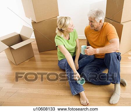 Couple sitting on floor among cardboard moving boxes drinking coffee View Large Photo Image Stock Image - Couple sitting on floor among cardboard moving boxes drinking coffee. Fotosearch