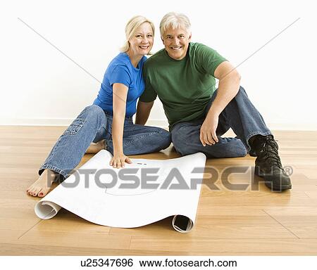 Stock Photograph - Couple sitting on floor with architectural blueprints. Fotosearch