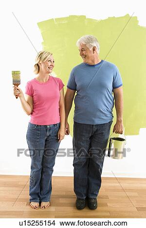 Picture - Couple standing in front of half-painted wall with paint supplies . Fotosearch