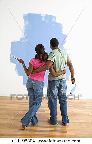 Picture - Couple standing together looking at half-painted wall. Fotosearch
