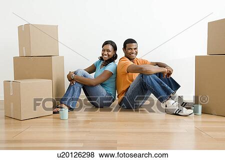 Stock Photo - Male and female couple sitting on floor next to moving boxes. Fotosearch