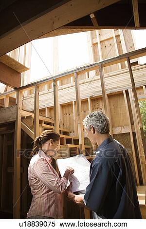 Stock Photography - Male and female with blueprints on building construction site. Fotosearch