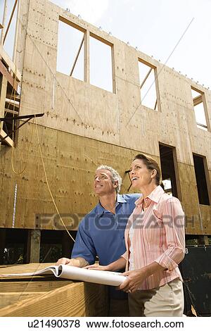 Stock Photo - Male and female with blueprints observing building construction site. Fotosearch