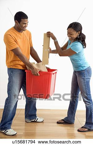 Picture - Male holding recycling bin while pretty female puts cardboard in. Fotosearch