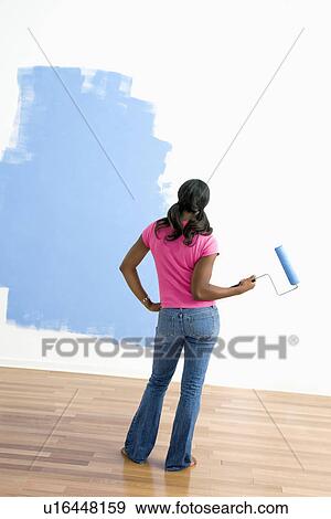 Woman standing next to half-painted wall with paint roller View Large Photo Image Stock Photo - Woman standing next to half-painted wall with paint roller. Fotosearch