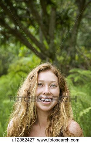 Stock Photo - Beautiful happy Caucasian young adult woman in lush forest smiling and looking at viewer.. Fotosearch
