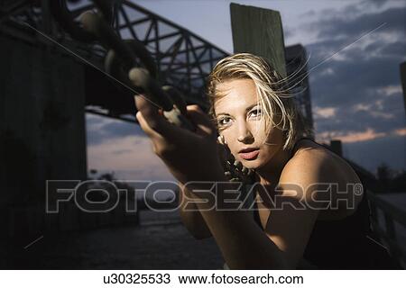Stock Image - Caucasian mid-adult blonde woman clinging to chain rail beside bridge.. Fotosearch