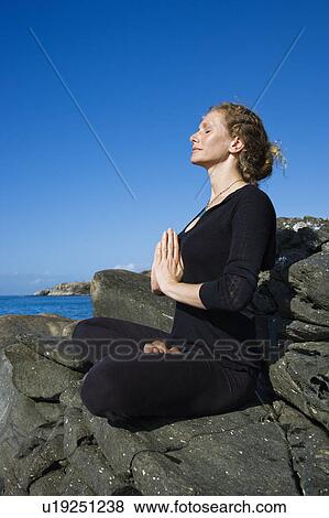 Stock Photo - Caucasian mid-adult woman practicing yoga on rocky coast of Maui, Hawaii.. Fotosearch