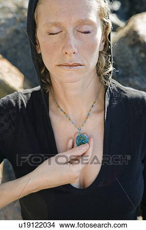 Caucasian mid-adult woman wearing black hoodie holding pendant necklace with eyes closed. View Large Photo Image Picture - Caucasian mid-adult woman wearing black hoodie holding pendant necklace with eyes closed.. Fotosearch